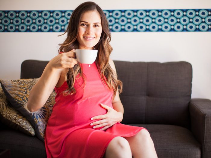 Pregnant woman sitting with a cup and looking into the camera