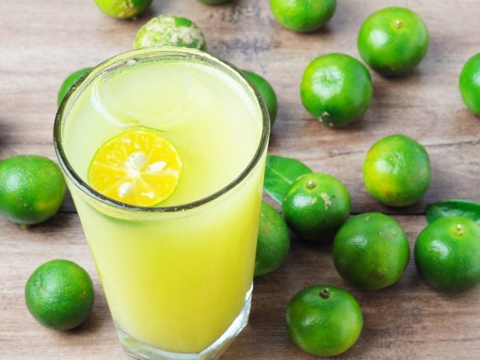 A glass of calamansi lime juice with fresh calamansi lime fruits on a wooden table
