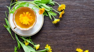 A flat lay picture of calendula tea placed on a black platform, surrounded by calendula flowers