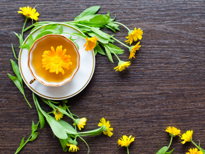 A flat lay picture of calendula tea placed on a black platform, surrounded by calendula flowers