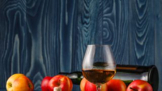A wine glass with calvados next to apples on a table counter