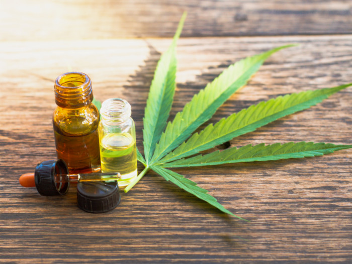 A bottle of cannabis essential oil and cannabis leaves on a table