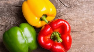 Different types of bell peppers and capsicum on a wooden table