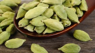 Green cardamom pods on a wooden spoon
