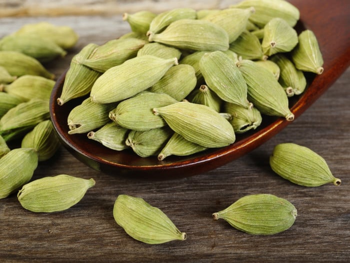 Green cardamom pods on a wooden spoon