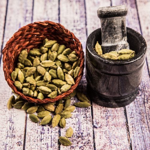 Cardamom cloves in a basket beside few in mortar & pestle