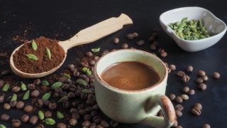 Black cardamom coffee in a cup, with coffee powder, cardamom pods, and coffee beans