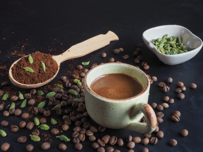 Black cardamom coffee in a cup, with coffee powder, cardamom pods, and coffee beans