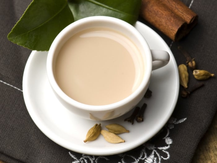 A teacup and saucer with cardamom tea with milk, and cardamom pods on the saucer