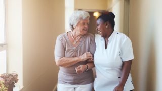 Happy female caregiver and senior woman walking together
