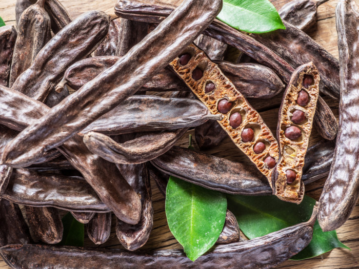 Carob pods and leaves of the carob tree on a wooden background