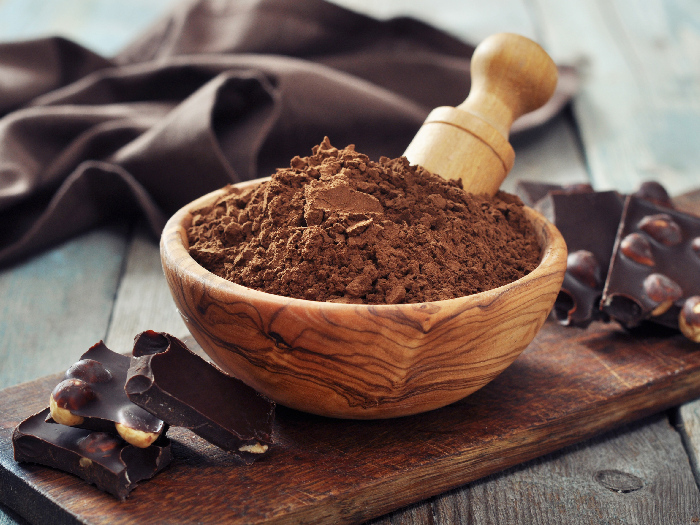 Carob powder in a bowl with chocolate pieces on wooden background