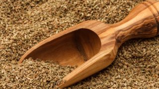 Close-up of dried carom seeds with a wooden scoop