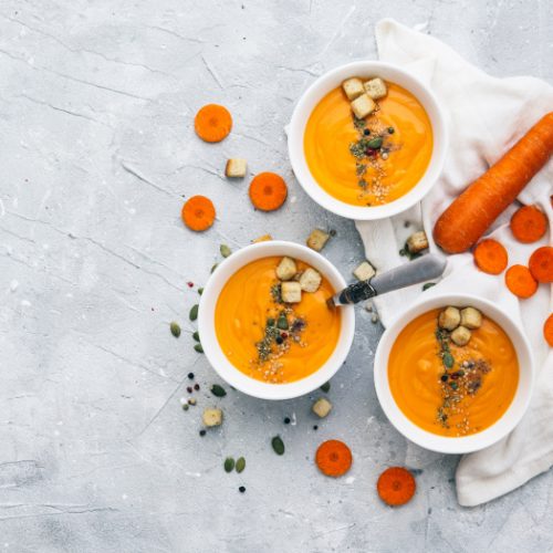 Three bowls of carrot and coriander soup topped with seeds and croutons