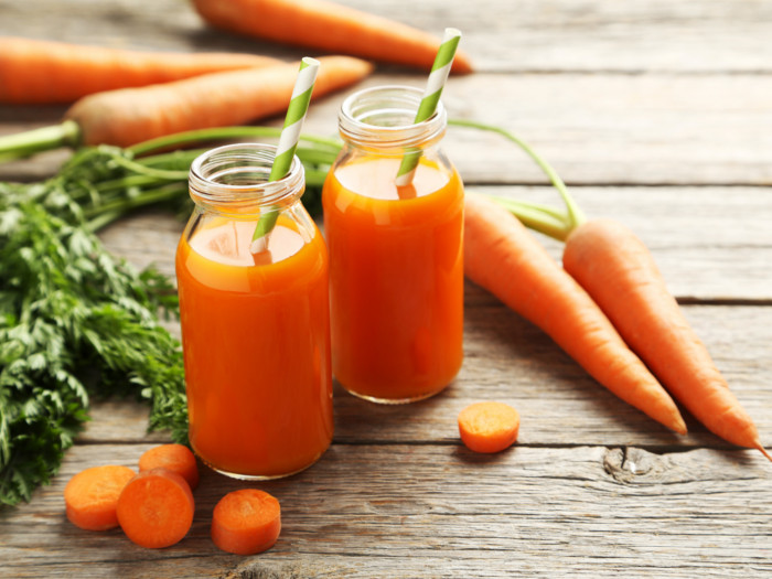 Carrots and two bottles of carrot juice on a wooden surface