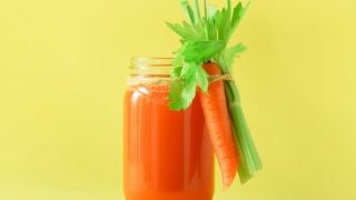 Fresh carrot with leaves tied on a jar of carrot juice on a yellow background