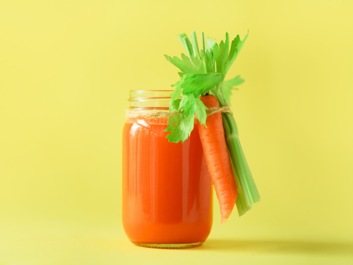 Fresh carrot with leaves tied on a jar of carrot juice on a yellow background