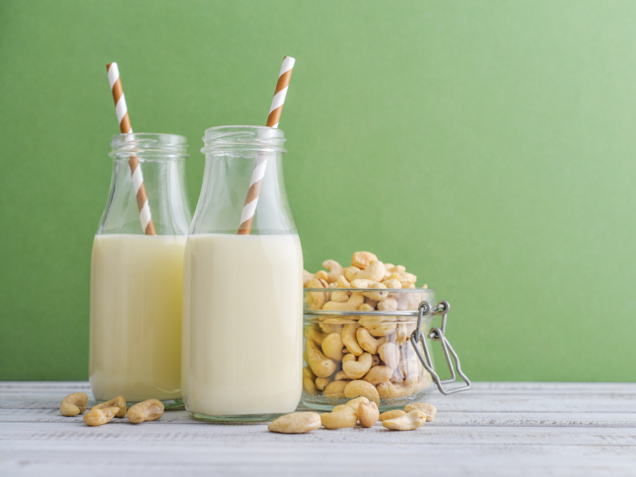 Two bottles of cashew milk with a jar of cashew nuts on a green background