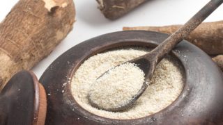 Cassava flour in a metal bowl surrounded by cassavas