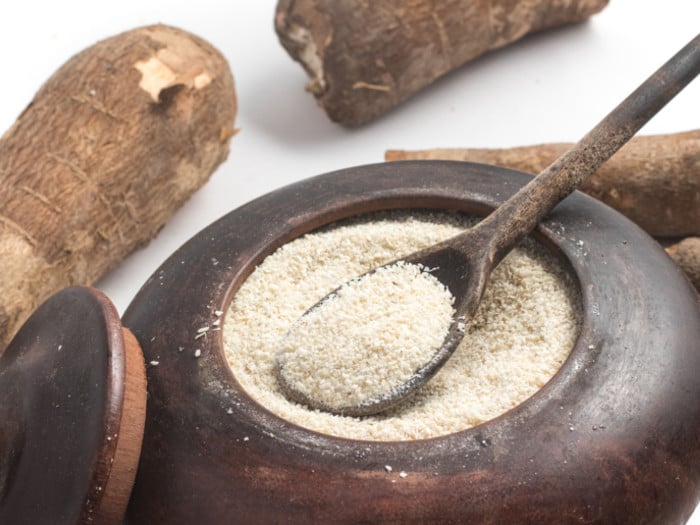 Cassava flour in a metal bowl surrounded by cassavas