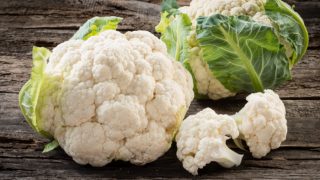 2 fresh raw cauliflower with green leaves on a wooden table