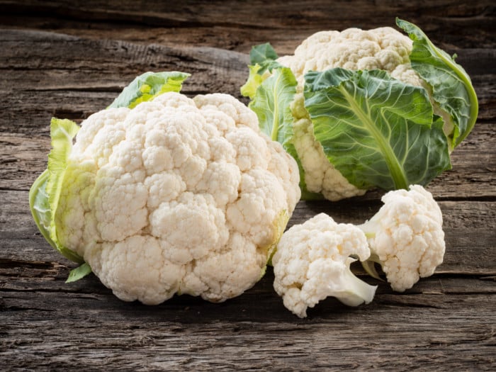 2 fresh raw cauliflower with green leaves on a wooden table