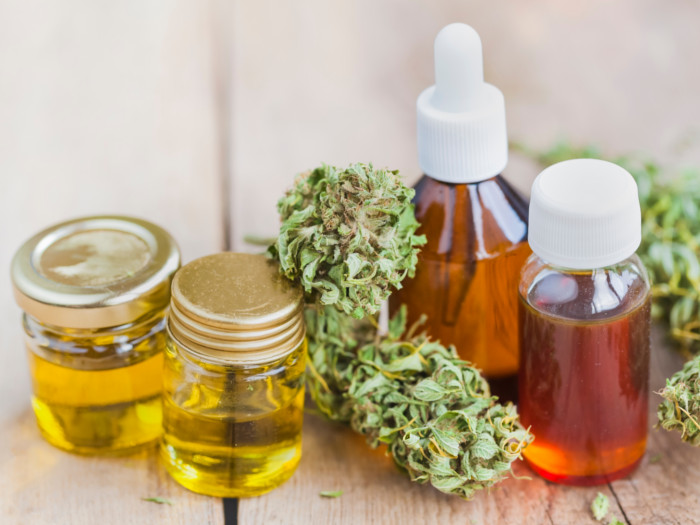 Bottles of cbd oil and hemp oil next to marijuana leaves on a wooden table