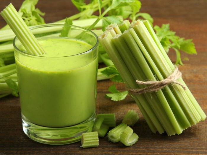 A glass of celery juice with a bunch of celery sticks on a wooden table