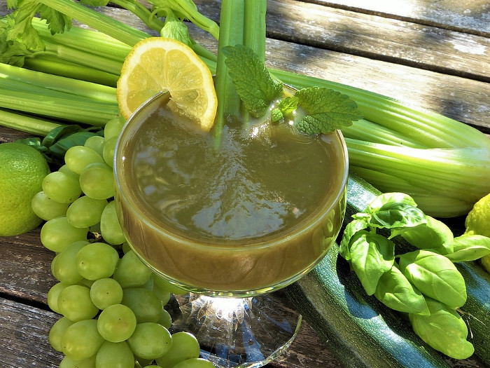 A glass of green smoothie made with celery, grapes, spinach, and mint on a table