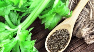 A wooden spoon with celery seeds next to celery leaves