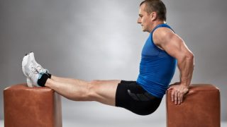 A man in gym clothes performing dips between two brown stools.
