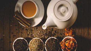 Flatline view of a kettle, a cup and saucer of tea with four small bowls of different spices.