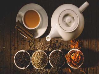 Flatline view of a kettle, a cup and saucer of tea with four small bowls of different spices.