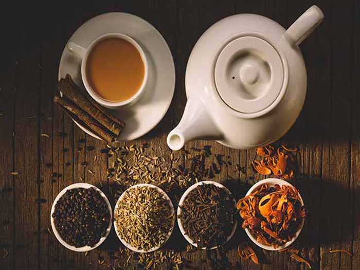 Flatline view of a kettle, a cup and saucer of tea with four small bowls of different spices.