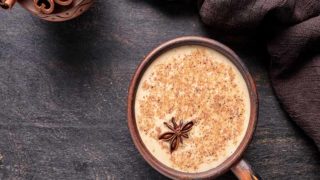 A cup of chai tea latte with cinnamon powder and star anise, with cinnamon sticks