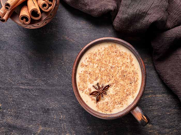 A cup of chai tea latte with cinnamon powder and star anise, with cinnamon sticks