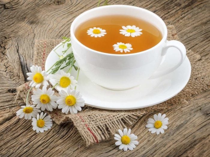 Chamomile tea in a white cup and chamomile flowers on a table