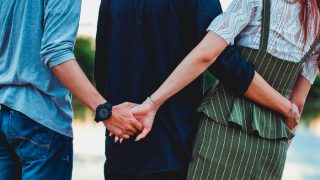 Two boys and a girl clicked from the back. The boy in the middle has arms around the girl's waist, while the other boy is holding the girl's hand behind his back.