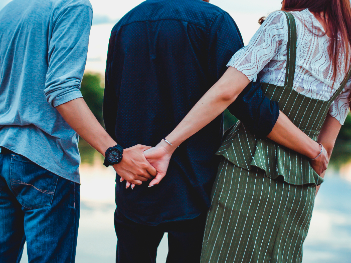 Two boys and a girl clicked from the back. The boy in the middle has arms around the girl's waist, while the other boy is holding the girl's hand behind his back.