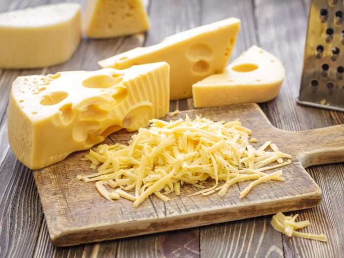 Grated and sliced fresh cheese on a chopping board on a wooden table