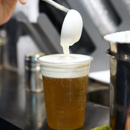 Pouring cream cheese to plastic glass of iced oolong tea with layer of cream cheese foam