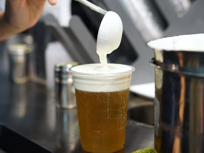 Pouring cream cheese to plastic glass of iced oolong tea with layer of cream cheese foam