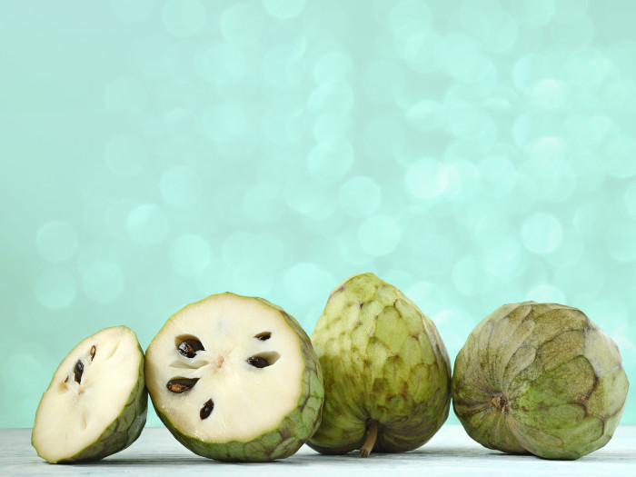 Two cut-up and two whole cherimoya fruits on a green background.