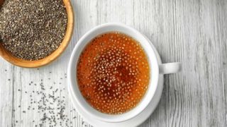 A flat lay pic of chia seed tea kept beside a bowl of chia seeds on top of a table