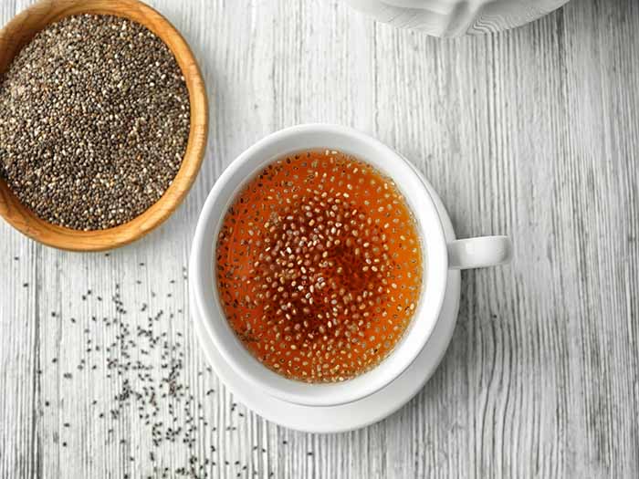 A flat lay pic of chia seed tea kept beside a bowl of chia seeds on top of a table