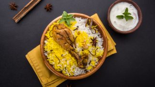 Flatline view of chicken biryani with yogurt dip on a slate background.