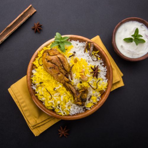 Flatline view of chicken biryani with yogurt dip on a slate background.