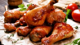 A closeup view of baked chicken legs on a paper with fresh tomatoes