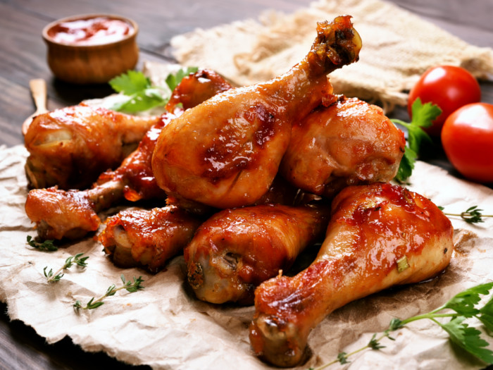 Un primer plano de unos muslos de pollo al horno sobre un papel con tomates frescos