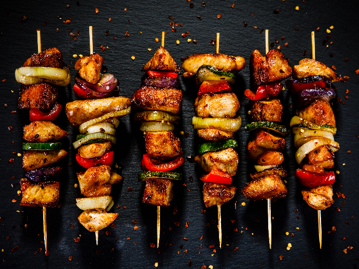 Chicken skewers with vegetables placed together on a black stone surface